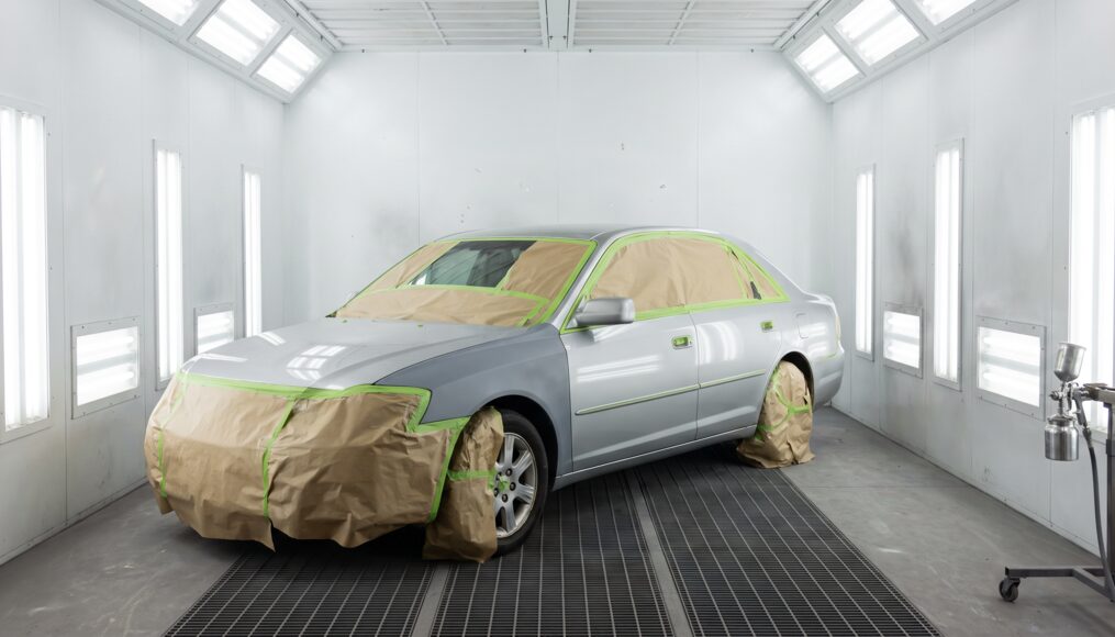 Sedan masked and staged inside a downdraft paint booth under bright lighting
