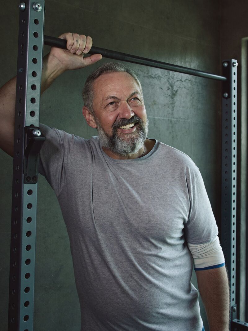 Ray Whitlock, strength coach, standing beside a squat rack with one hand on the upright