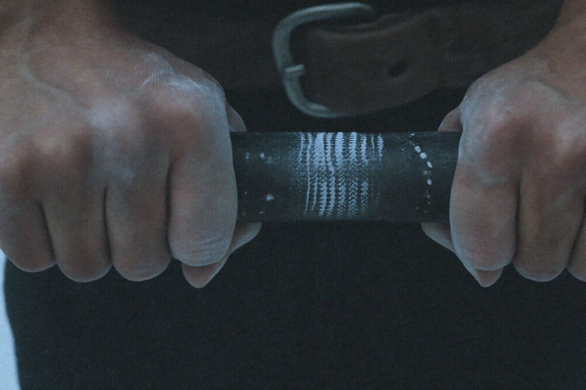 Two chalked hands gripping the knurling of a loaded barbell resting in a rack