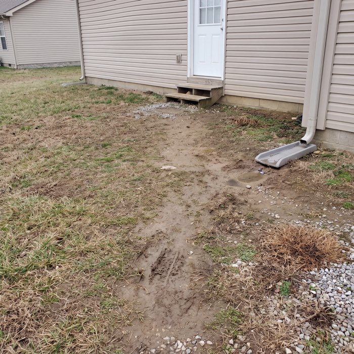 Before: bare compacted dirt and a worn footpath outside the back door, a downspout discharging onto open soil