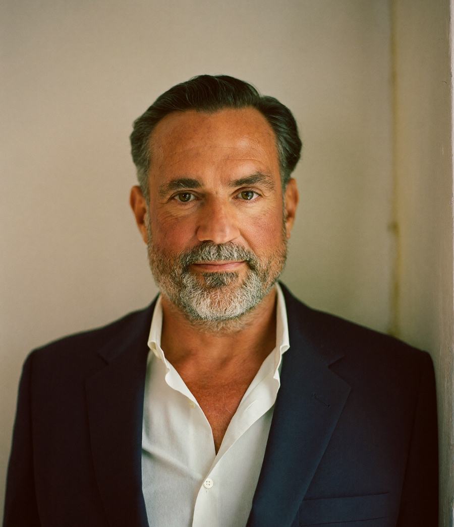 Jonah Vale, partner — a man in a navy blazer and open-collar white shirt against a warm plaster wall.