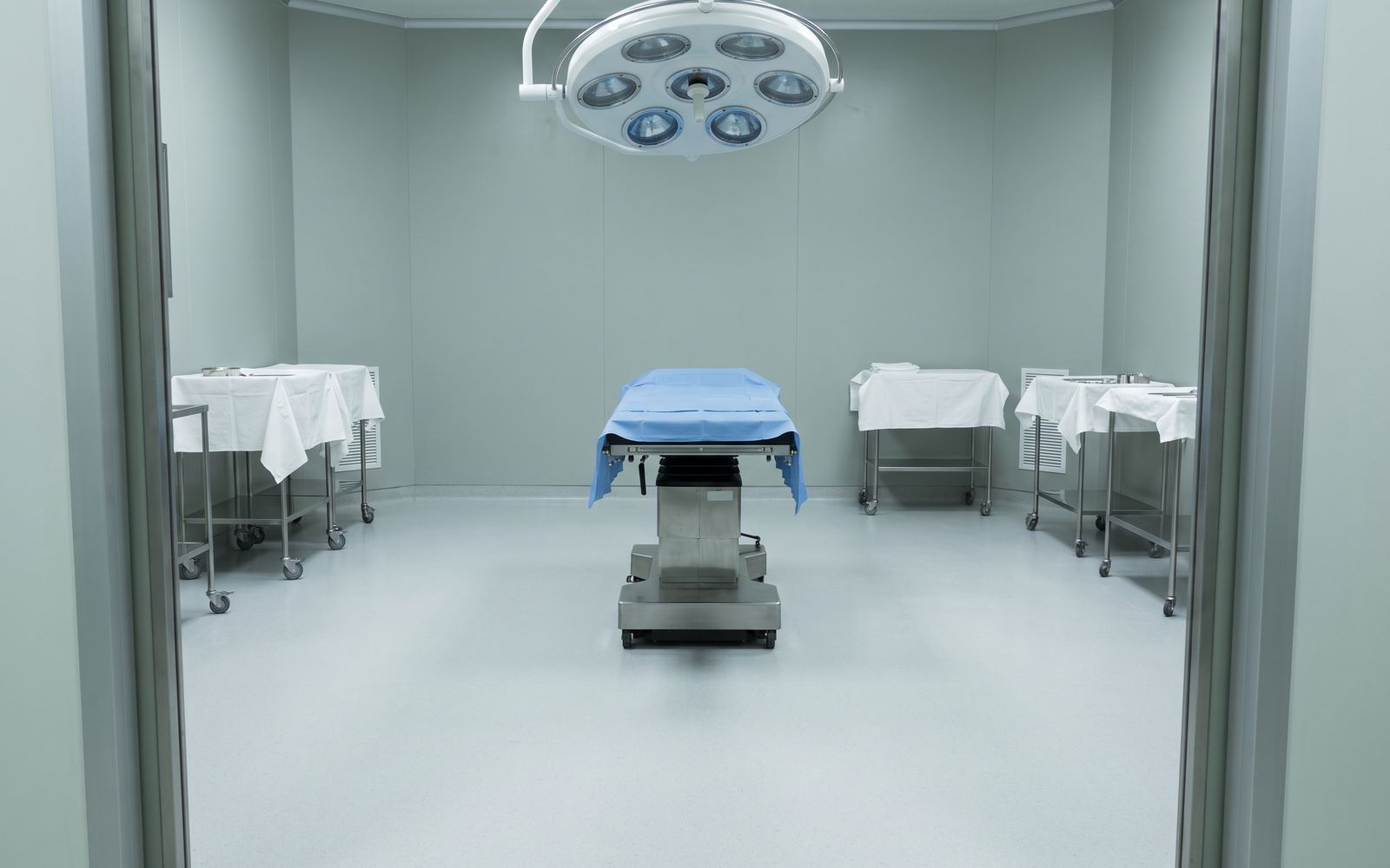 The practice's on-site operating room, prepared and empty: bare table, overhead light array switched off, draped instrument trolleys