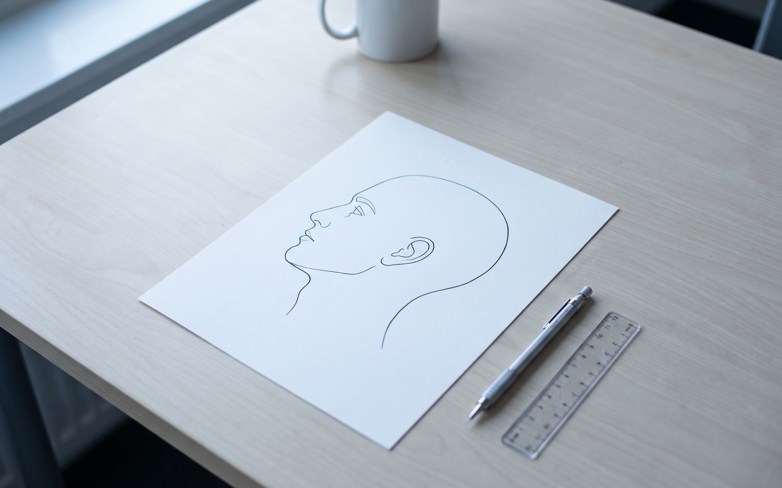 A consultation table with a surgical profile study drawn in a single continuous line on plain paper, a mechanical pencil and a ruler beside it
