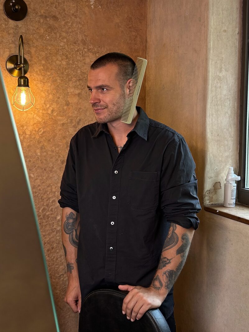 Dev Marchetti standing at his barbering station, comb behind his ear