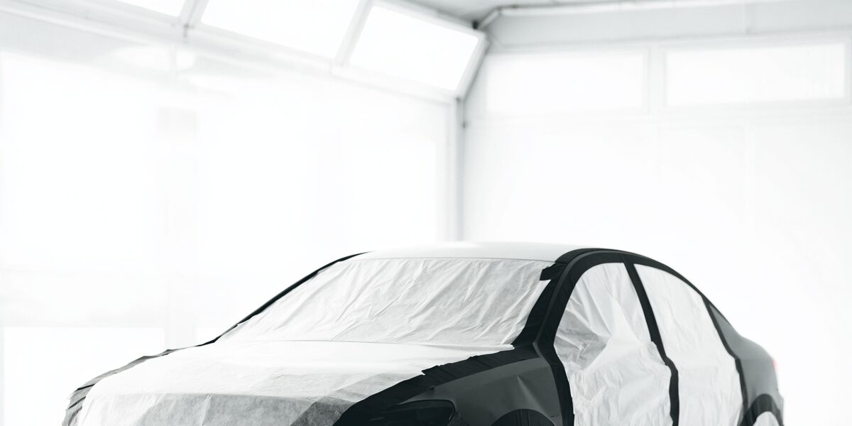A sedan masked for paint in a bright, modern body-shop paint booth